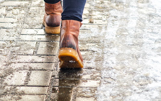 a person wearing snow boots walking on a icy sidewalk