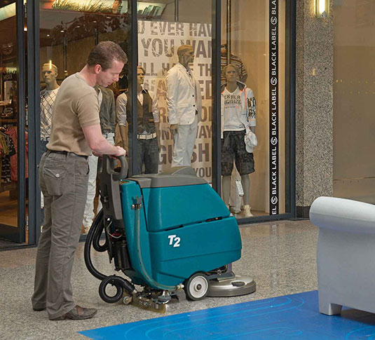une équipe de nettoyage utilisant la récureuse à plancher à commande arrière de Tennant dans la zone principale du magasin de détail